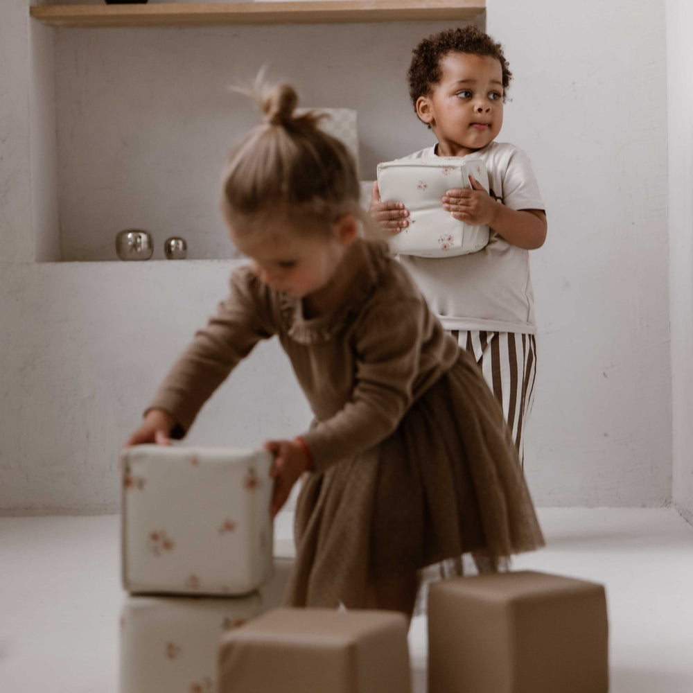 Twee kinderen spelen samen met zachte stapelblokken in floral en taupe.