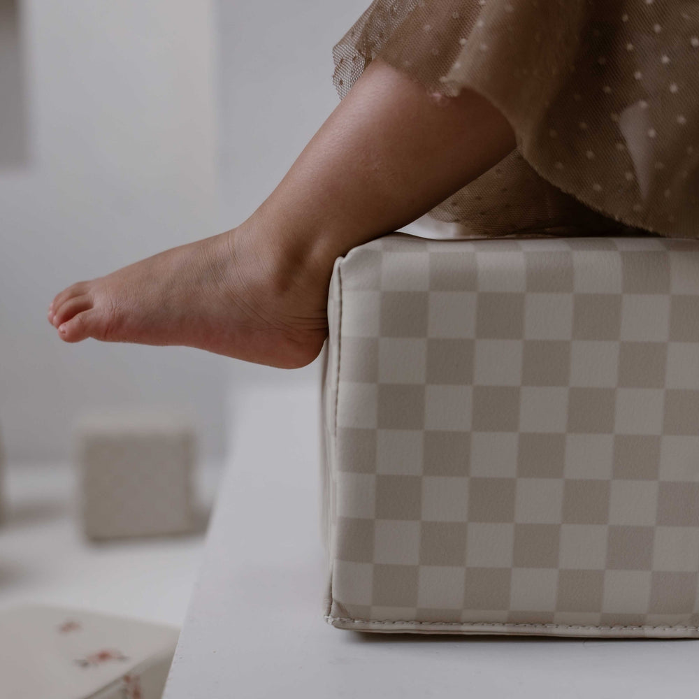 Close-up van een kind op een zacht beige stapelblok met geblokt patroon