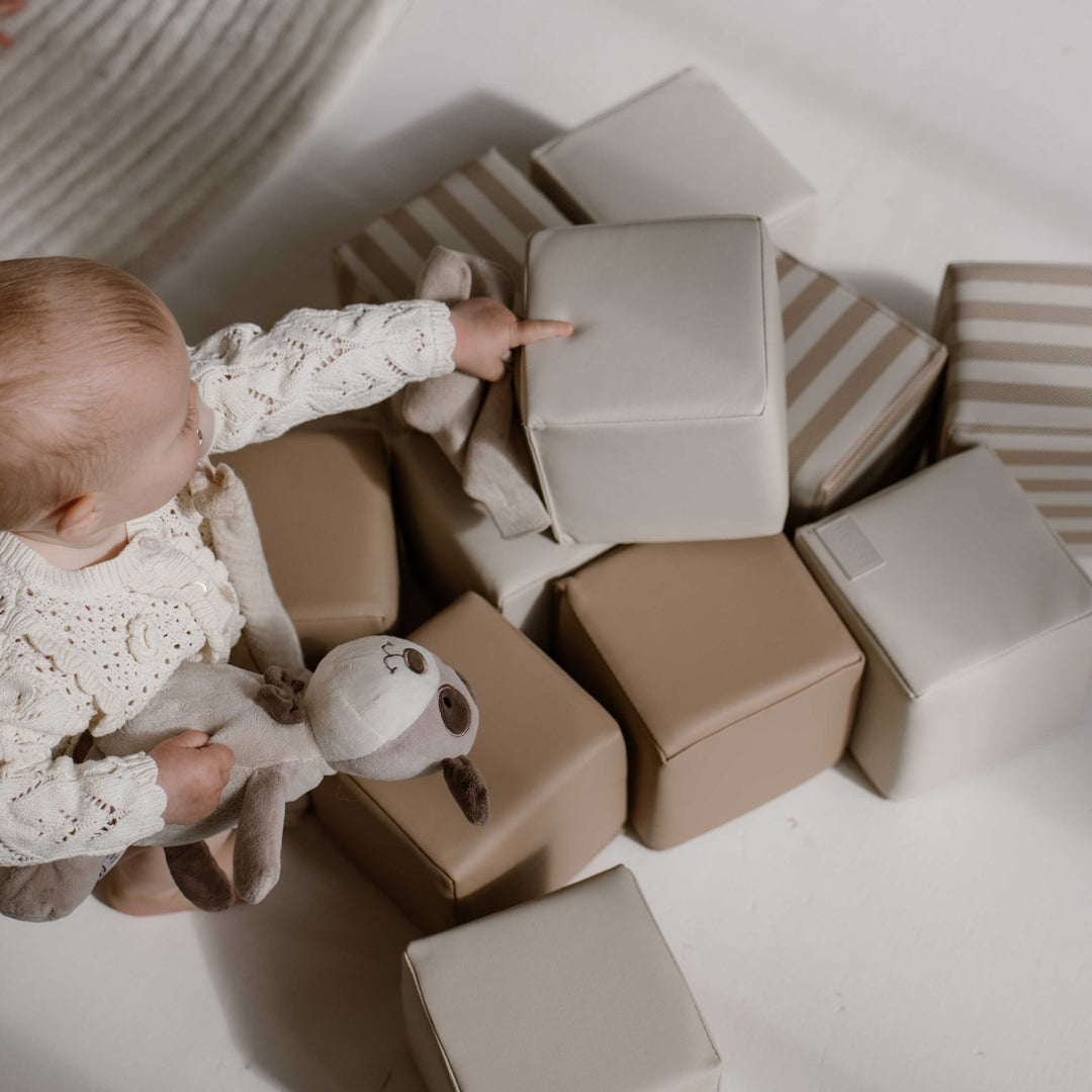 Baby speelt tussen zachte stapelblokken in beige, taupe en streepjesdesign