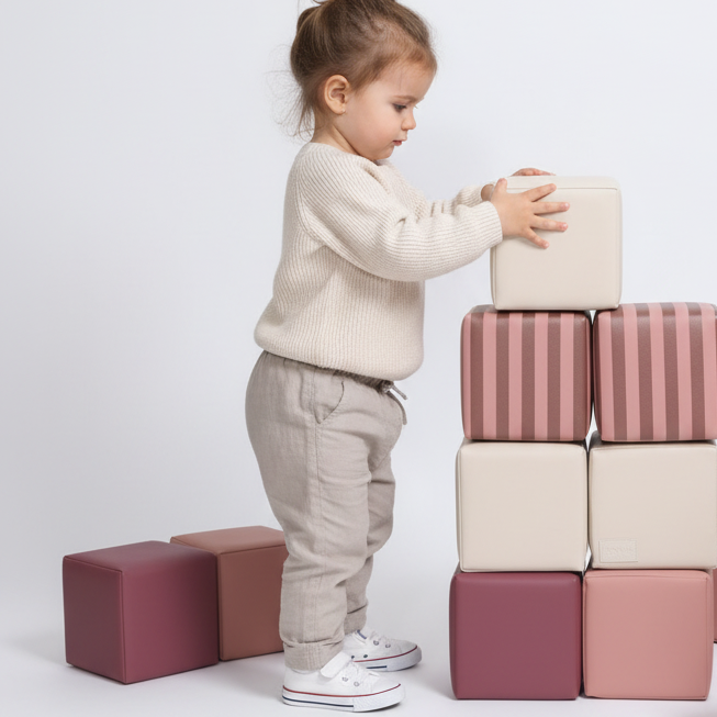 Kind speelt met gestreepte HENVAE stapelblokken in roze, beige, merlot en Merlot Rose.