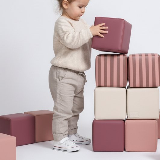 Kind speelt met gestreepte HENVAE stapelblokken in roze, beige, merlot en Merlot Rose.
