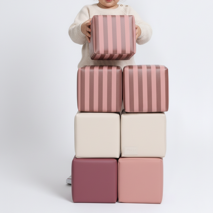 Kind speelt met gestreepte HENVAE stapelblokken in roze, beige, merlot en Merlot Rose.