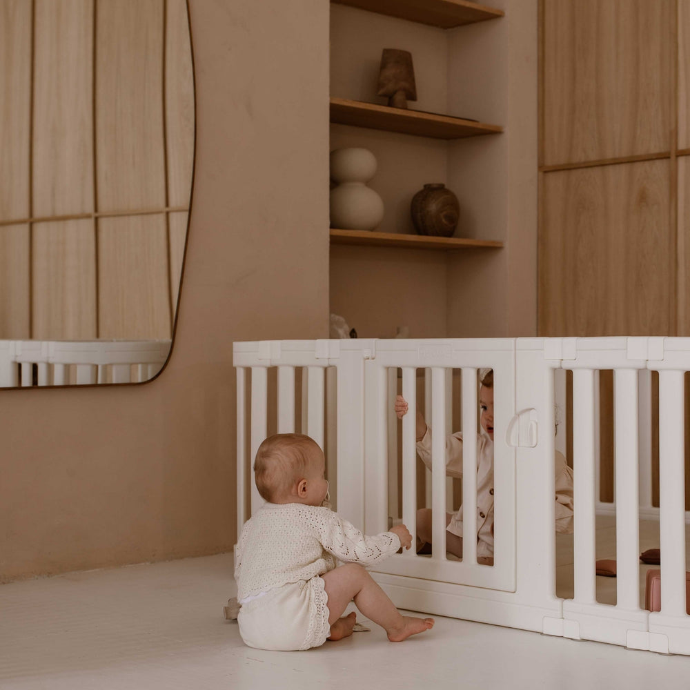 Twee baby’s maken contact door de spijlen van de offwhite groundbox