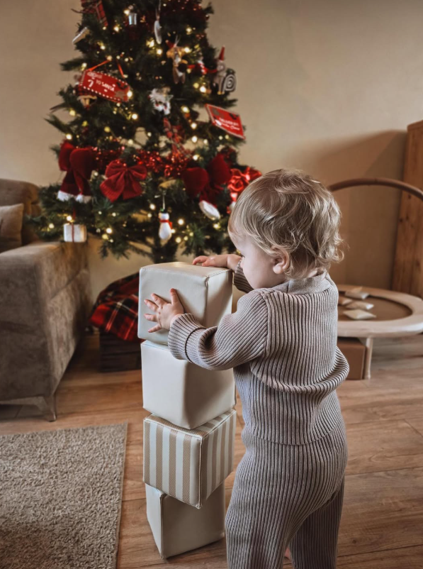 Peuter stapelt zachte blokken bij de kerstboom