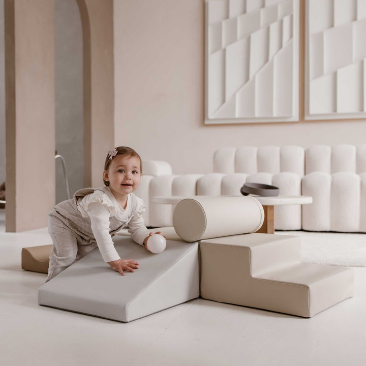 Kind klimt over de zachte glijbaan van de beige baby speelset